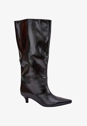 Botte noire en cuir brillant, montante jusqu'au genou, avec un bout pointu et un petit talon, inclinée vers la droite sur fond blanc.