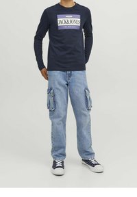 Navy long-sleeve T-shirt with white and purple logo print paired with light blue cargo jeans featuring side pockets and dark sneakers.