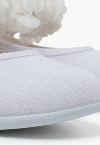 Ballerine bianche in tela con superficie texture, suola piatta e fiori decorativi in tessuto bianco sui lati.