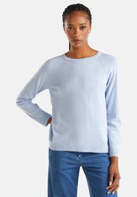 Pull en tricot bleu clair en tissu doux, avec de longues manches raglan et un col rond. Présente des poignets et un ourlet côtelés.