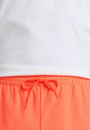 T-shirt en coton blanc au-dessus de shorts à taille élastique orange vif avec cordon de serrage. Les shorts présentent un bandeau élastique froncé et un nœud.