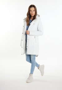 Hvid parka jakke med hætte, lynlåslommer og trykknaplukninger. Bæres over en blå top og kombineres med lyseblå jeans og beige højhælede sneakers.