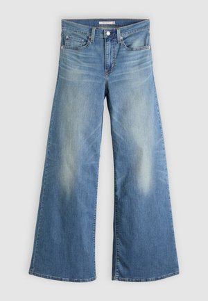 Jean large couleur bleu clair en denim. Présente une taille haute, des poches avant et un délavage au niveau des cuisses. Détail d'ourlet brut.