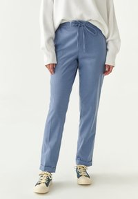 Lichtblauwe, taps toelopende broeken met een trekkoord in de taille en zijzakken, gecombineerd met crèmekleurige sneakers met donkerblauwe accenten.