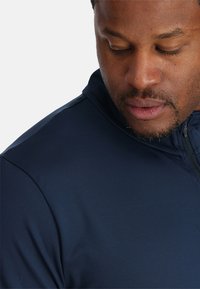 Marineblaue Zip-Jacke aus dehnbarem Material, mit hohem Kragen und glatter Textur. Enthält keine sichtbaren Muster oder Akzente.