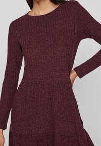Vínová, dlouhá šaty s jemně drážkovanou strukturou a rozšířenou sukní. Obsahuje kulatý výstřih a přiléhavý živůtek.