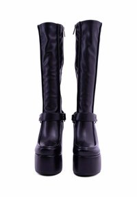 Stivali alti neri in finta pelle con una superficie liscia, dotati di una cerniera laterale e di una cinghia decorativa alla caviglia con dettaglio della fibbia. Suola spessa e piattaforma.