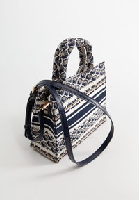 Kuvioitu kangaskassi, jossa on tummansininen ja valkoinen raitakuosi, yhdistettynä sileisiin sinisiin nahkaketjuihin ja lyhyisiin kahvoihin. Mukana myös pitkä olkahihna.