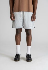 Light gray mesh shorts with a loose fit, white drawstring, and contrasting trim, paired with black decorative loafers and white socks.