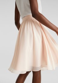 Een knie-lange, lichtroze rok gemaakt van lichtgewicht, vloeiende stof met een gerimpelde taille en gelaagde textuur. Reikt boven de knie.