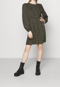Robe à imprimé léopard en tissu vert olive, avec des manches longues bouffantes et une jupe évasée, associée à des bottes de combat noires à lacets.
