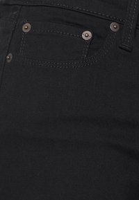 Jeans de ganga pretos com uma textura suave, design de cinco bolsos e detalhes de costura subtis. Acentos de metal estão presentes nos bolsos.