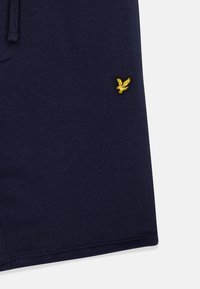 Marineblaue Baumwollshorts mit einem gestickten gelben Adler-Logo. Der Stoff hat eine glatte Textur und einen Bund mit Kordelzug.