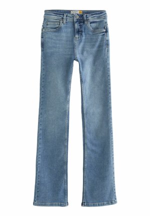 Mujer con jeans azul claro, top corto blanco, chaqueta plateada con lentejuelas y sandalias beige con tacón caminando sobre un fondo azul claro.