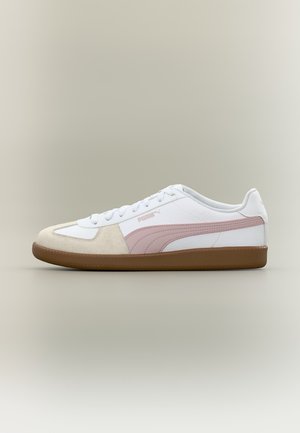 Biały i beżowy sneaker Puma z różowym paskiem po boku i brązową podeszwą, widziany z zewnętrznej strony na neutralnym tle.