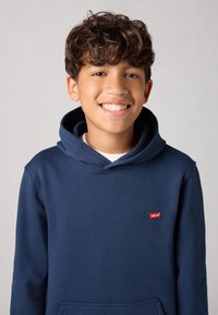 Sweat-shirt à capuche bleu marine en tissu doux avec une poche kangourou et une patch logo rouge Levi's sur la poitrine. Dispose d'une coupe décontractée.