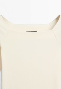 Cream-colored top with a wide, square neckline and short sleeves shown from the upper chest to shoulders.
