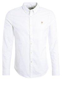 Camisa blanca de botones con cuello clásico, mangas largas y un pequeño logo dorado en el pecho. Fabricada con un tejido suave y Woven.