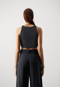 Černý krajkový crop top s vysokým výstřihem a bezrukávovým designem, doplněný černými kalhotami s vysokým pasem a boční kapsou.