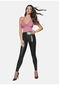 Różowy top na halter z kokardą w detalu, zestawiony z czarnymi, błyszczącymi legginsami o wysokim stanie. Modelka ma na sobie czarne, szpiczaste szpilki. Całość ma gładką fakturę.