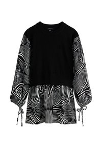 Schwarzer kurzer Strickpullover, der über einer schwarz-weißen Bluse mit abstraktem Muster, Ballonärmeln und Bindebändern getragen wird.