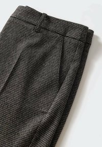 Gros plan d’un pantalon habillé à motif pied-de-poule gris et noir, avec passants de ceinture et pli latéral, posé à plat sur une surface blanche.