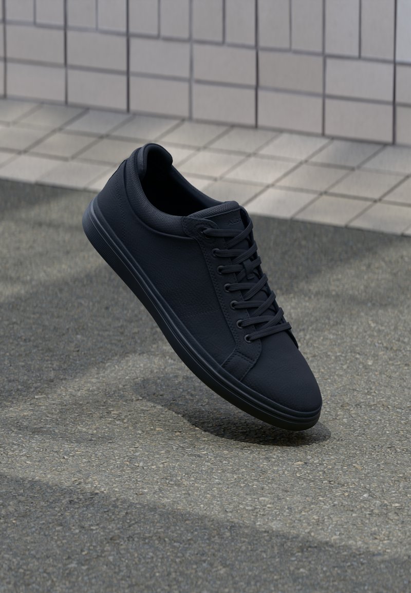 Black textured sneakers with a rounded toe, flat laces, and a minimalist design. The sole is smooth and slightly elevated.