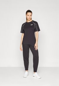 Conjunto atlético preto composto por uma t-shirt com detalhes brancos e calças de jogging a condizer, acompanhadas por sapatilhas brancas. O material parece macio e respirável.