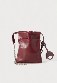 Burgundy leather drawstring bag with smooth texture, chain strap, and small circular accent. Minimalist design, soft draped top.
