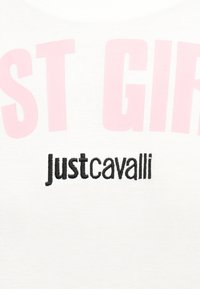 Άσπρο ύφασμα με ροζ μερικό κείμενο "ST GIR" και μαύρο κεντητό λογότυπο "Just Cavalli" κάτω από αυτό.