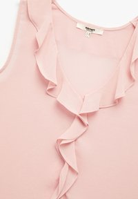 Pehmeä vaaleanpunainen hihaton pusero, jossa on pyöreä kaula-aukko. Etuosassa on pystysuora röyhelöyksityiskohta, joka on tehty kevyestä kankaasta.