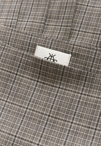 Bruin geruit stof met een gestructureerde weving en een wit label met een zwart logo in een van de hoeken.