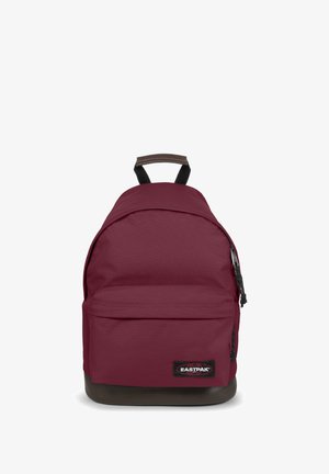 Bordeauxfarbener Rucksack mit runder Form, vorderer Reißverschlusstasche, strukturiertem braunem Boden und verstellbaren Schultergurten. Logopatch auf der Vorderseite.