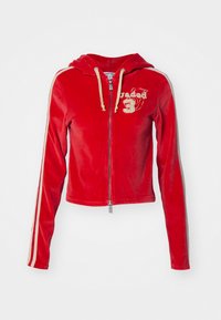 Punainen samettinen lyhythihainen huppari, jossa on beige naru, vetoketjukiinni, ja valkoiset sivusuorat. Rinnassa brodeerattu logo.