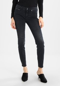 Černé skinny džíny s hladkou texturou, s kolenními panely, středně vysokým pasem a jemnými švy. Spárováno s černými muly.