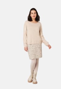Beige Langarmpullover, strukturierter Strick, kombiniert mit einem gesprenkelten creamfarbenen Bleistiftrock. Getragen mit hellbeigen Schnürstiefeln.