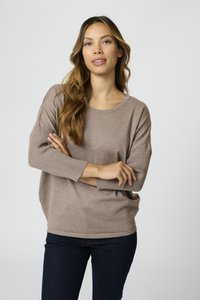 Løs beige striktrøje med lange ærmer, bred halsudskæring og ribbede detaljer. Kombinationen med mørkeblå jeans, minimal tekstur og simpelt design.