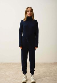 Mörkblå stickad tröja med hög hals och långa ärmar, tillsammans med matchande joggers med elastisk midja och muddar vid anklarna.