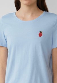 Lichtblauwe katoenen t-shirt met een ronde hals. Heeft een kleine geborduurde aardbei op de linkerborst. Korte mouwen.