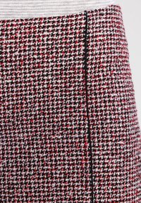 Jupe tissée dans un motif pied-de-poule rouge, noir et blanc. Présente une taille lisse et une couture latérale épurée avec des détails en noir.