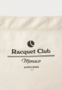 Plátenná taška v prírodnej farbe s čiernym potlačeným textom. Obsahuje "Racquet Club Monaco," tenisový symbol a "BJÖRN BORG 1956."