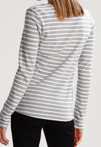 Maglietta a maniche lunghe grigia con strisce orizzontali bianche. Tessuto morbido, design aderente, scollatura rotonda e cuciture piatte. Pantaloni neri visibili in basso.