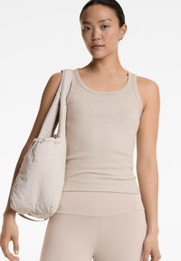 Beige geripptes Tanktop mit rundem Halsausschnitt; kombiniert mit einer weichen Schultertasche mit Zugband in einem passenden hellbeigen Farbton.