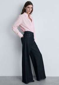 Camicia a righe rosa chiaro con bottoni abbinata a jeans in denim blu scuro a vita alta e gamba larga. Include tasche e cuciture distintive.