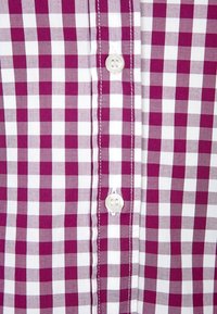 Camicia a quadri viola e bianca con chiusura a bottoni sul davanti e bottoni in plastica, caratterizzata da una superficie liscia in cotone e un motivo costante.