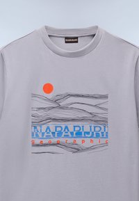 T-shirt en coton gris clair avec un design graphique comportant des lignes ondulées, un cercle orange et le texte "NAPAPIJRI geographic" en bleu et rouge.