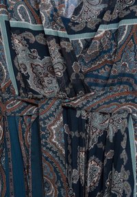 Tissu bleu foncé avec des motifs cachemire et floraux complexes en marron, bleu sarcelle et blanc, avec une ceinture nouée autour de la taille.