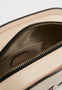 Inuti en krämfärgad läderhandväska, med ett beige foder och svart dragkedja. Inkluderar en liten logotagg inuti.