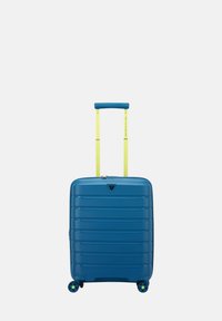 Valigia rigida blu con linee orizzontali testurizzate, manico retrattile giallo e quattro ruote blu per una facile mobilità.
