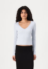 Light blue long-sleeve top with a ribbed texture and lace trim along the deep V-neckline, paired with a fitted black skirt.